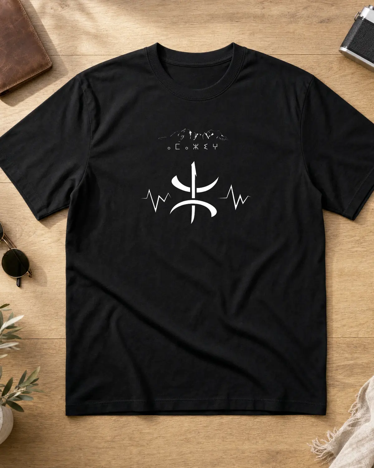 Black Amazigh t-shirt front with large white Yaz ⵣ symbol crossed by a heartbeat line, an Atlas ridge and Tifinagh script above