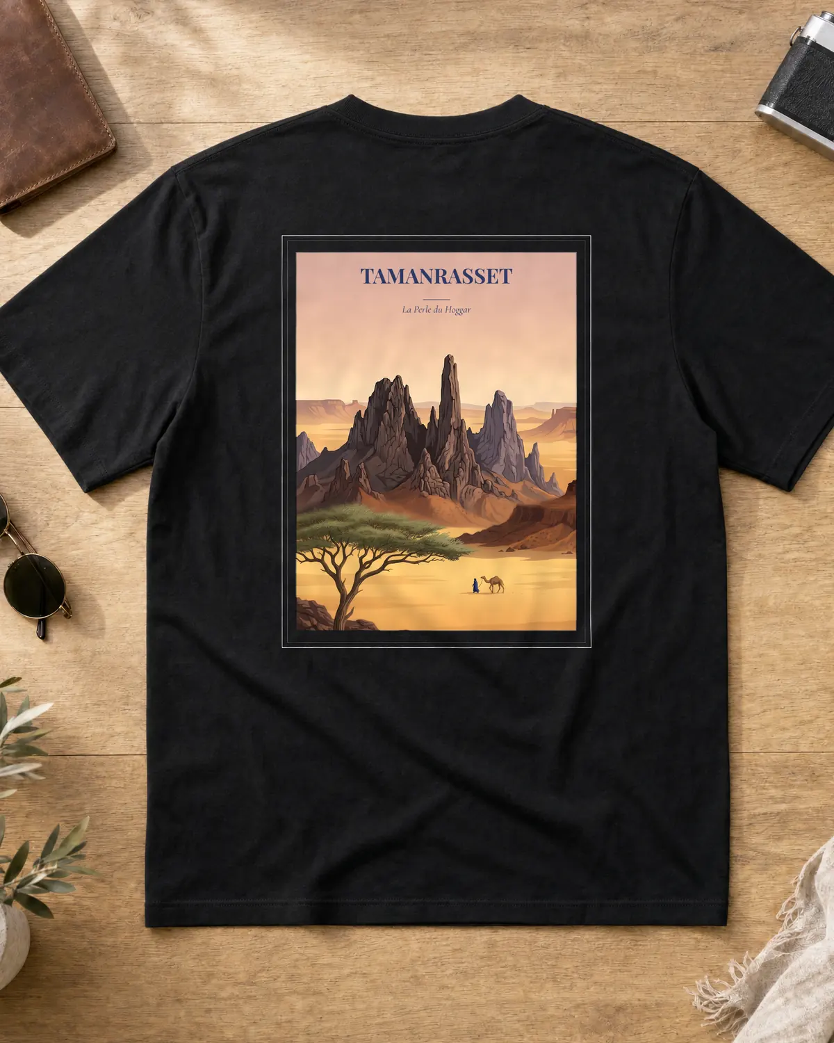 Black Tamanrasset t-shirt back with vintage travel poster — volcanic Hoggar spires at dusk, a lone acacia, and a Tuareg leading a camel across the Sahara